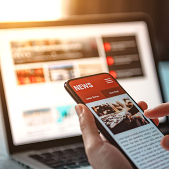 a person with news on their phone and a laptop in the background